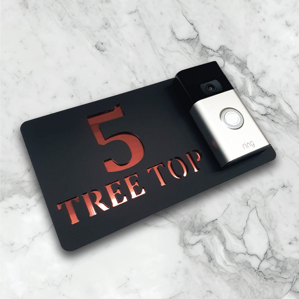 Black house sign with a video doorbell on showing text and street address in a black and rose gold finish