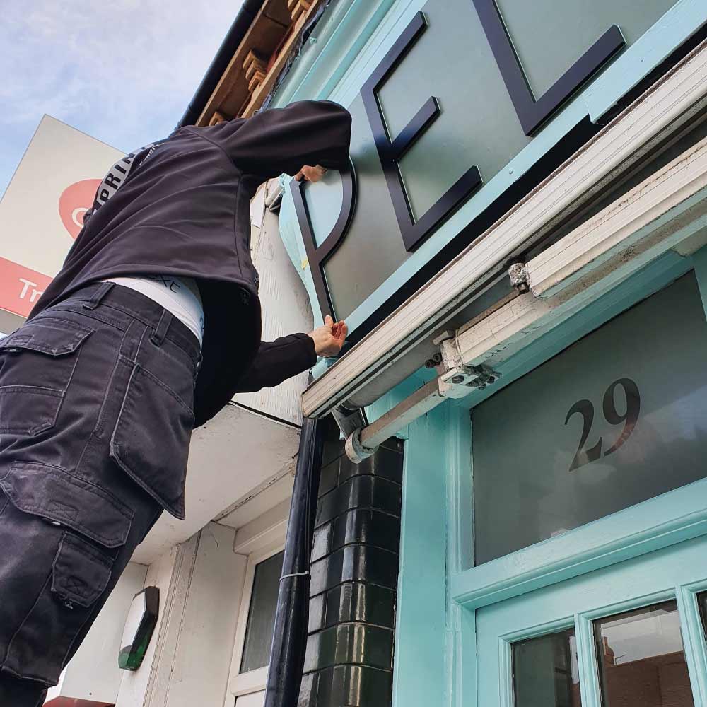 a man applying a 3d acrylic lettering logo a cut letter logo on a outside of a building