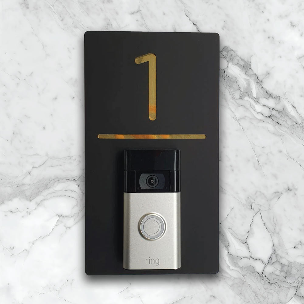 Black vertical house sign with gold details with an added video ring doorbell on face of house sign