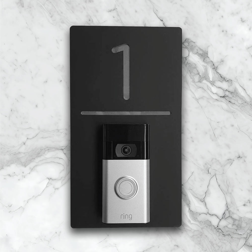 Black vertical house sign with silver details with an added video ring doorbell on face of house sign